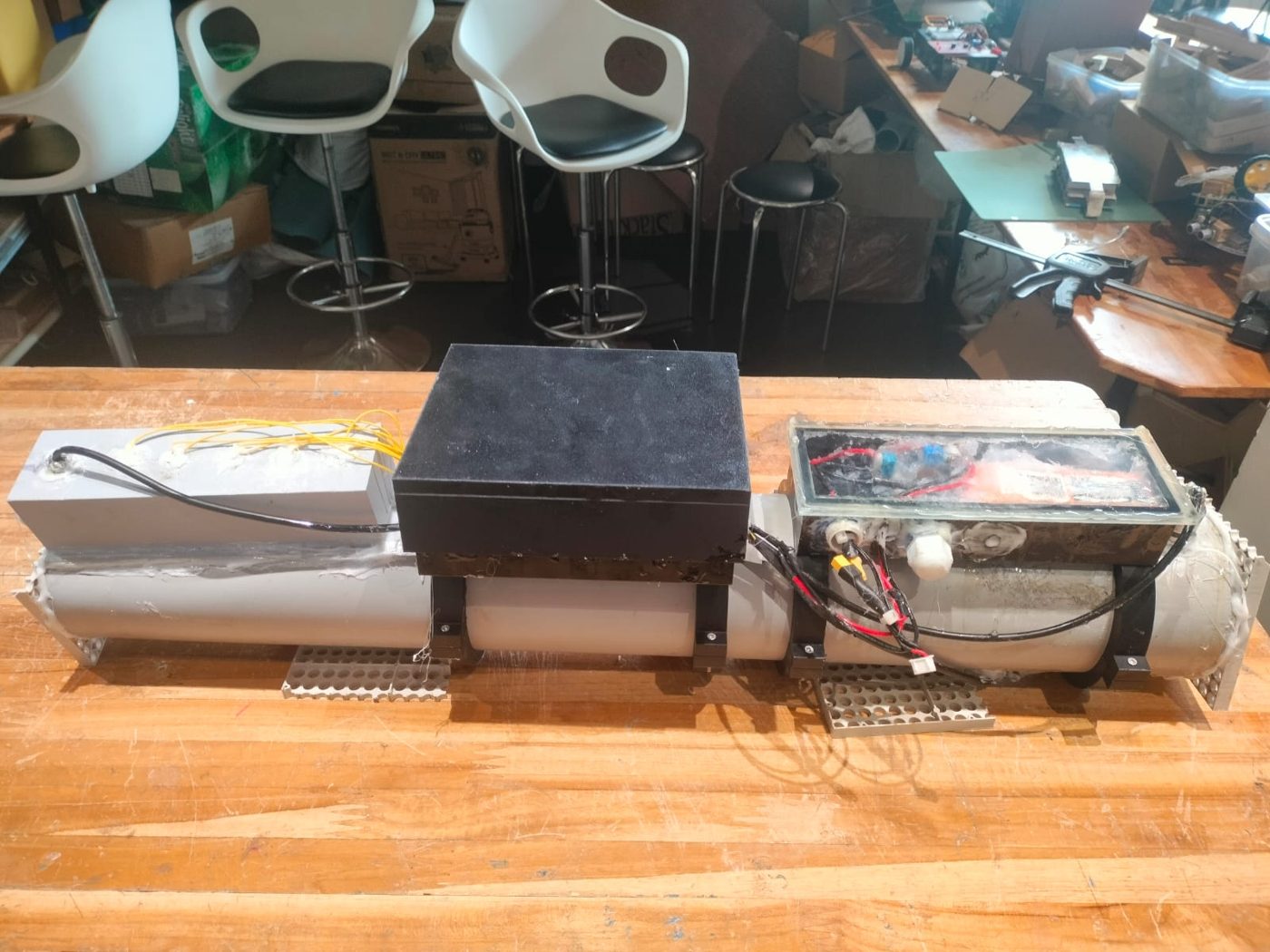 The FloodGuard prototype on a workshop bench: a black sensor housing and a clear electronics box mounted on a section of drain pipe